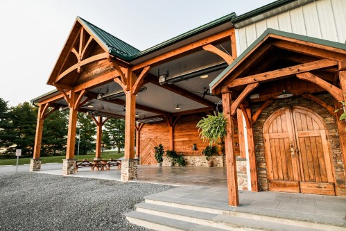 A rustic wooden building with a green roof, featuring a spacious porch and stone accents, surrounded by greenery.