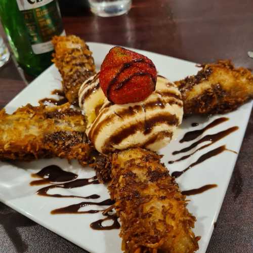 A plate with four fried desserts, topped with a scoop of ice cream and a strawberry, drizzled with chocolate sauce.