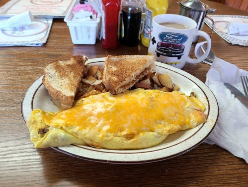 A plate with a cheese omelet, toast, and hash browns, alongside a coffee cup on a wooden table.