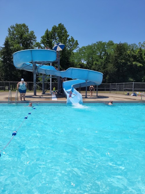 A sunny pool scene with a water slide, people swimming, and lounging by the poolside.