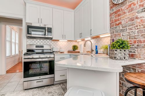 Modern kitchen with white cabinets, stainless steel appliances, and a brick accent wall, featuring a small dining area.