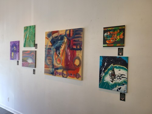 A gallery wall displaying colorful abstract paintings in various styles and sizes.