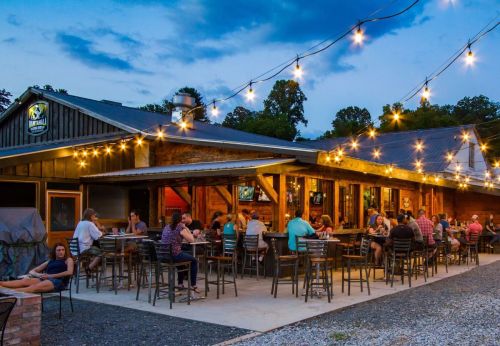 A lively outdoor restaurant with string lights, featuring diners enjoying food and drinks on a warm evening.