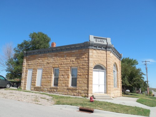Historic stone bank building with a rounded entrance, set against a clear blue sky and green grass.