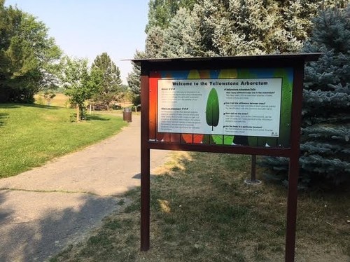 Sign at the Yellowstone Arboretum welcomes visitors, with colorful background and information about the site. Pathway visible.