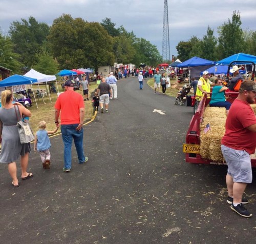 A bustling outdoor market scene with people walking, tents set up, and a red trailer in the foreground.