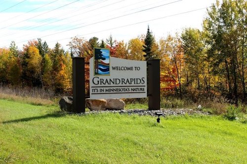 Welcome sign for Grand Rapids, Minnesota, surrounded by colorful autumn trees and grassy landscape.