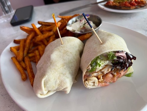 A plate with two wrapped sandwiches and a side of sweet potato fries, accompanied by a small bowl of dipping sauce.