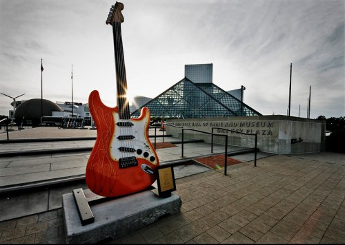 Giant orange guitar sculpture in front of the Rock and Roll Hall of Fame, with a glass building in the background.