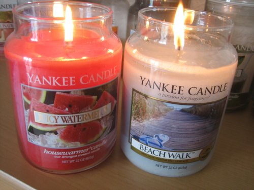 Two Yankee Candle jars: one red labeled "Juicy Watermelon" and one white labeled "Beach Walk," both with lit wicks.