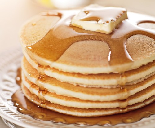 A stack of fluffy pancakes topped with a pat of butter and drizzled with syrup on a decorative plate.