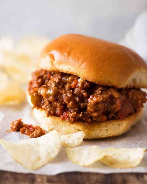 A hearty sloppy joe sandwich on a bun, served with potato chips on the side.