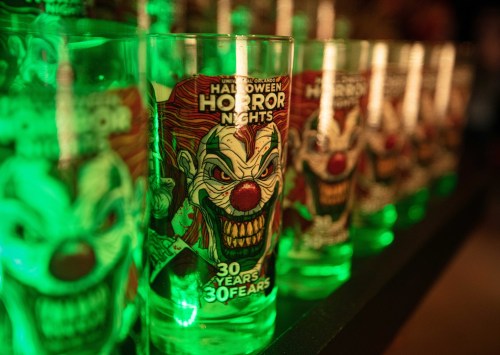 A row of glowing green shot glasses featuring creepy clown designs for Halloween Horror Nights.