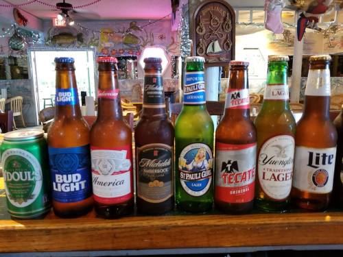 A variety of beer bottles and cans lined up on a bar, including Bud Light, Tecate, and O'Doul's.
