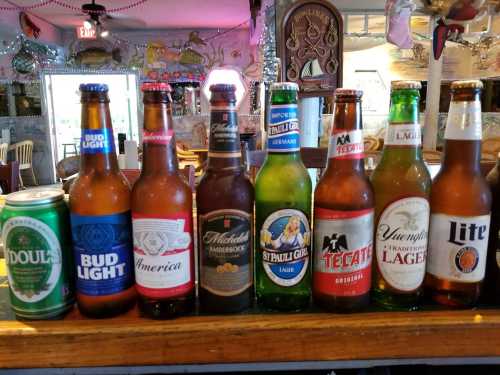 A variety of beer bottles and cans lined up on a bar, including Bud Light, Tecate, and O'Doul's.