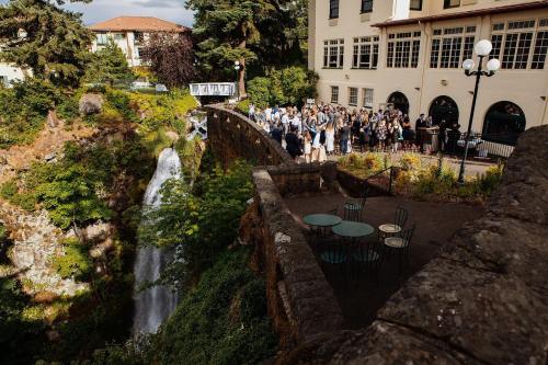 A group of people gathered near a waterfall, with a building and greenery in the background.