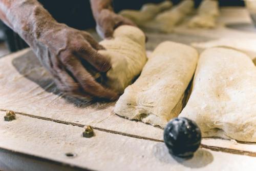 A baker's hands knead and shape dough on a floured wooden surface, with loaves lined up nearby.