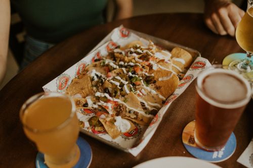 A platter of nachos topped with cheese, jalapeños, tomatoes, and drizzled with sour cream, served on a wooden table.