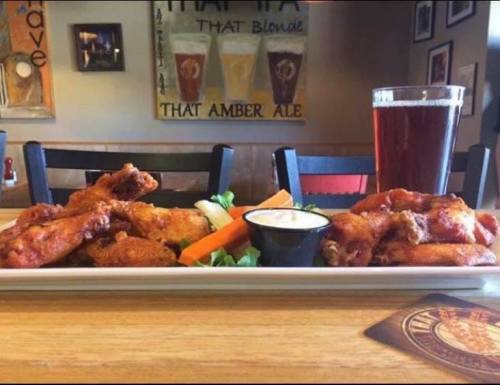 A platter of crispy chicken wings with carrots, celery, and dipping sauce, alongside a glass of amber beer.