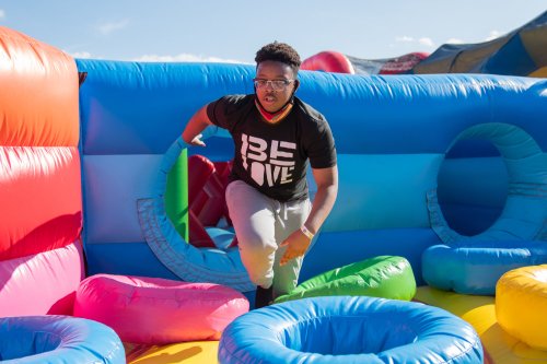 A person in a black "BE LOVE" shirt plays on a colorful inflatable structure, navigating through bright rings.