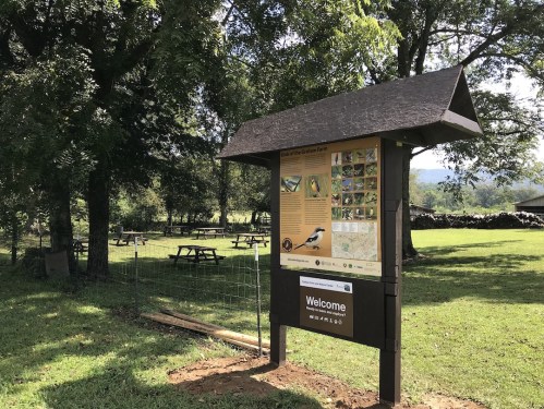 A welcome sign at a garden farm, with picnic tables in the background and trees surrounding the area.