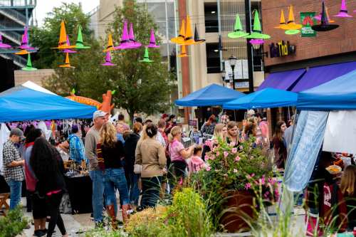 A bustling outdoor market with colorful tents, people browsing, and festive decorations overhead.