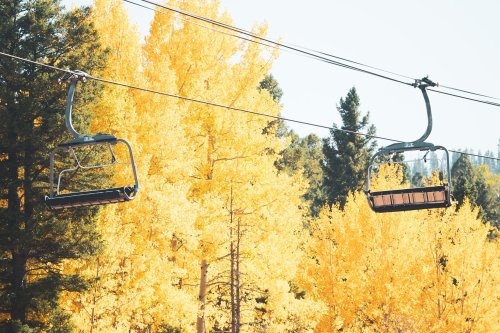 Two empty ski lift chairs suspended above vibrant yellow autumn trees.