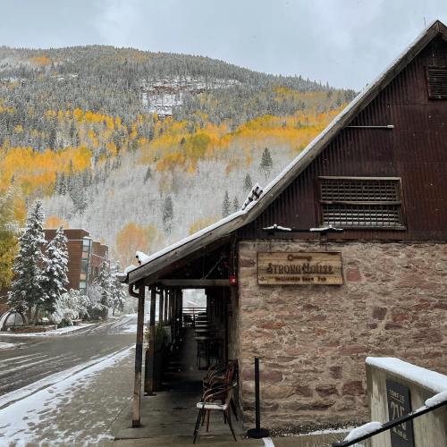 A rustic building with a stone facade, surrounded by snow and autumn-colored trees on a mountain.