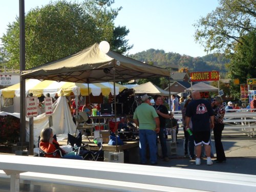 A bustling outdoor event with tents, food stalls, and people socializing in a sunny setting.