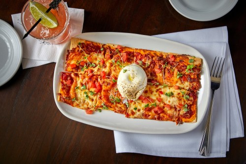 A rectangular pizza topped with cheese, tomatoes, and herbs, served with a dollop of cream on a white plate.
