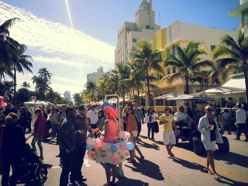 A busy street scene in a tropical setting with people, palm trees, and colorful decorations.