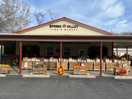 A market building with a sign reading "Spring Valley" and wooden crates filled with fresh produce outside.