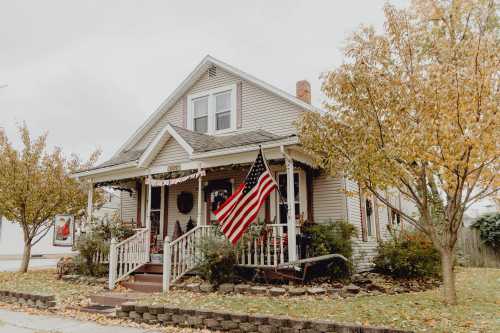 A charming house with a front porch, American flag, and autumn foliage surrounding it.