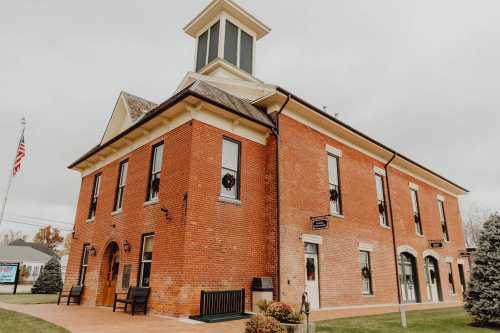 Historic red brick building with a clock tower, decorated with wreaths, surrounded by greenery and an American flag.