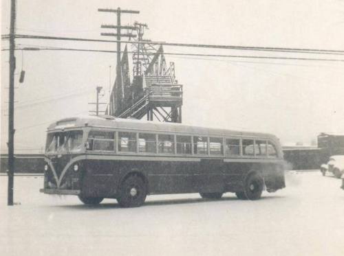 A vintage bus parked in a snowy landscape, with power lines and a structure in the background.