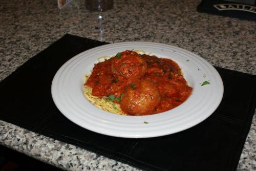 A plate of spaghetti topped with meatballs and marinara sauce, garnished with herbs, on a granite countertop.
