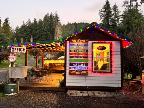 A cozy office building decorated with colorful lights, featuring a welcoming sign and surrounded by trees.