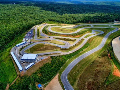 Aerial view of a winding racetrack surrounded by lush green forests and hills.