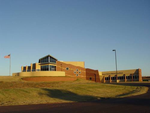 Modern building with large windows, set on a grassy hill, featuring a flagpole and circular design elements.