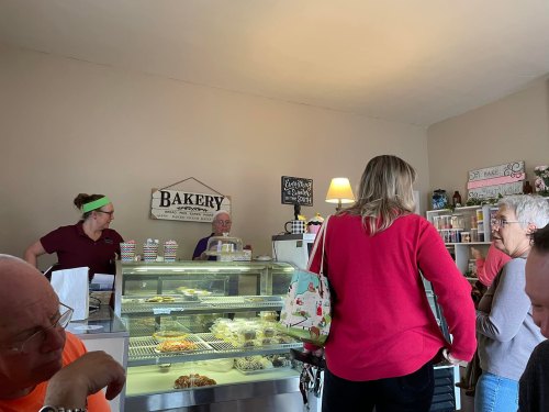 A cozy bakery interior with customers at the counter and a display of pastries. Staff members assist patrons.
