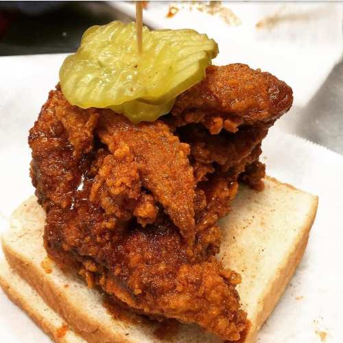 A crispy fried chicken piece on white bread, topped with a pickle slice and a toothpick.