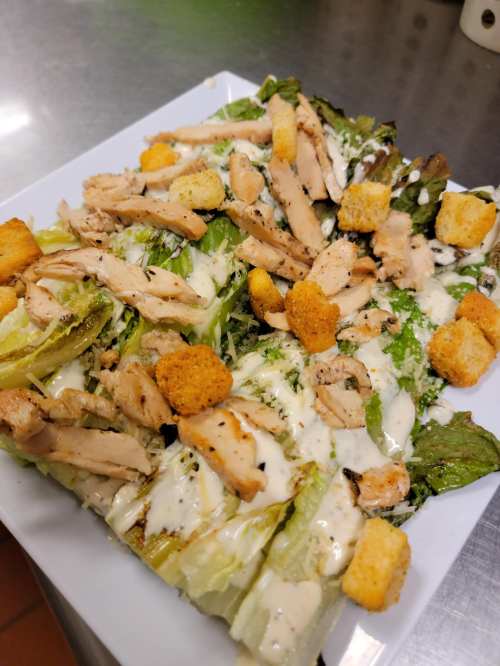 A fresh salad with romaine lettuce, grilled chicken, croutons, and creamy dressing on a white plate.