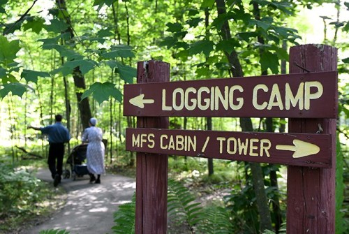 Signpost directing to a logging camp and MFS cabin/tower, with two people walking on a wooded path.