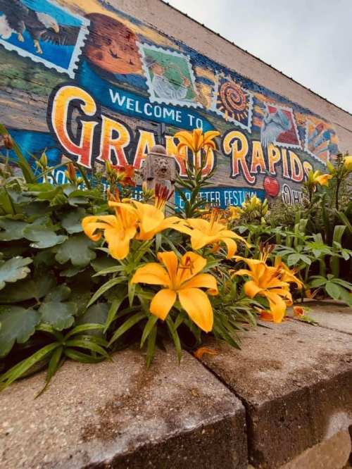 Colorful mural reading "Welcome to Grand Rapids" with vibrant yellow lilies in the foreground.