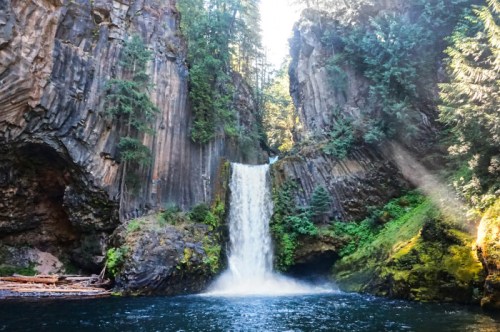 A serene waterfall cascades into a clear pool, surrounded by towering rock formations and lush greenery.