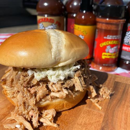 A pulled pork sandwich topped with coleslaw, surrounded by various bottles of barbecue sauces and spices.