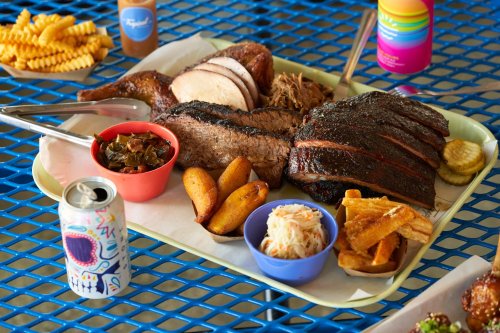 A colorful tray of barbecue meats, sides, and drinks on a blue table, featuring brisket, chicken, and various sides.