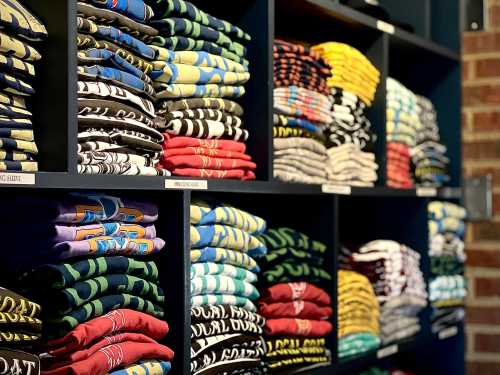 A neatly organized display of colorful folded t-shirts on shelves, showcasing various designs and patterns.