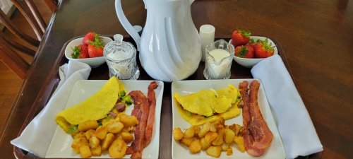 A breakfast tray with two plates of omelets, bacon, and potatoes, alongside strawberries and a pitcher of milk.