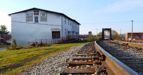 A railway track curves beside a weathered building with signs, set against a clear sky and grassy area.